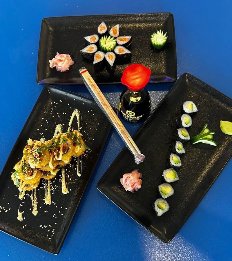 Black plates of maki, avocado rolls and crispy tempura sushi